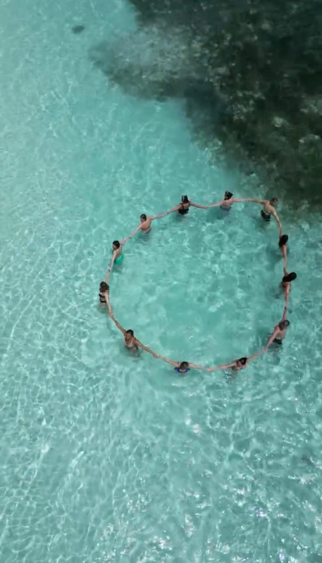 Retreat group holding hands in a circle in clear Maldives water